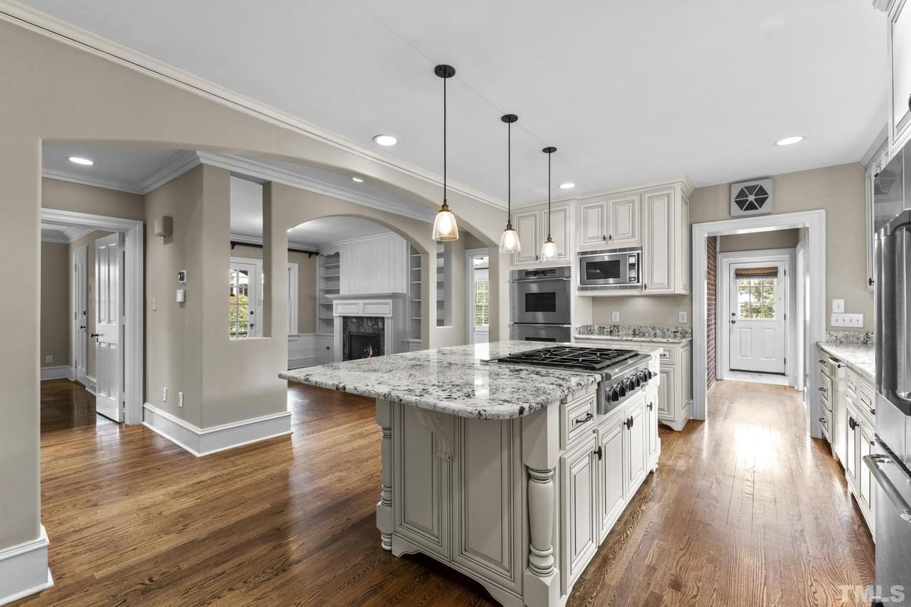 A classy kitchen with natural wood floor, black and white granite countertops, carved wooden columns, and white cabinetry